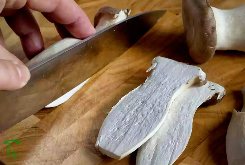 برش طولی قارچ شاه صدف با چاقو روی تخته چوبی